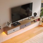 Scandinavian-style floating TV cabinet with white and gray drop-down doors and cable management