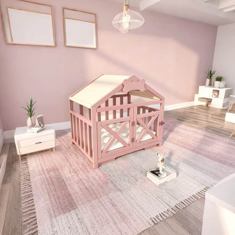 A cozy pink wooden indoor dog house with a pitched roof, featuring vertical grille slats, a cream fabric canopy, a white plush tufted cushion, and an open front with a small bone-shaped accent.