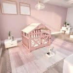 A cozy pink wooden indoor dog house with a pitched roof, featuring vertical grille slats, a cream fabric canopy, a white plush tufted cushion, and an open front with a small bone-shaped accent.